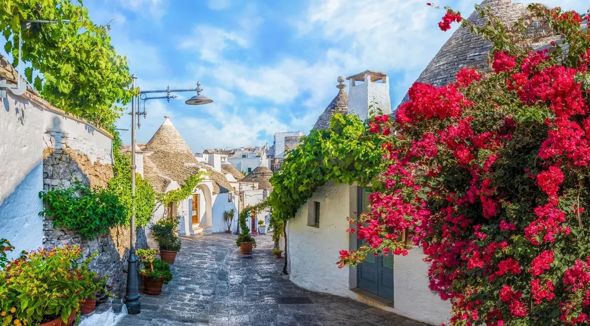 Flowers and white trulli along a stone lane